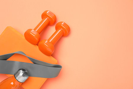 Dumbbells, thermo bottle, fitness elastic band and yoga block on coral background, flat lay. Space...