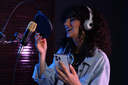 Vocalist with smartphone singing into microphone in professional record studioの写真素材