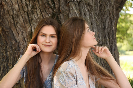 Two beautiful twin sisters near tree outdoorsの写真素材