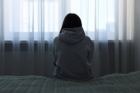 Loneliness concept. Sad woman sitting on bed at homeの写真素材