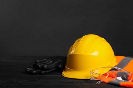 Reflective vest, hard hat, protective gloves and goggles on black wooden surface against gray background, space for textの写真素材