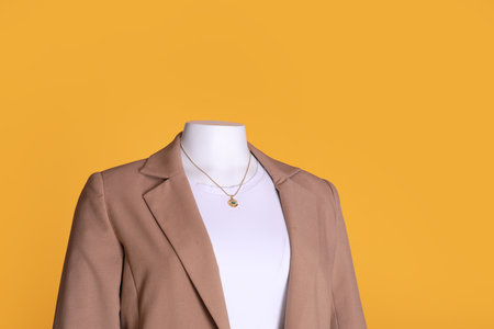 Female mannequin dressed in white t-shirt with necklace and stylish jacket on orange backgroundの写真素材