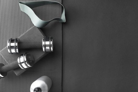 Dumbbells, yoga block, mat, thermo bottle and fitness elastic band on black background, flat lay. Space for textの写真素材