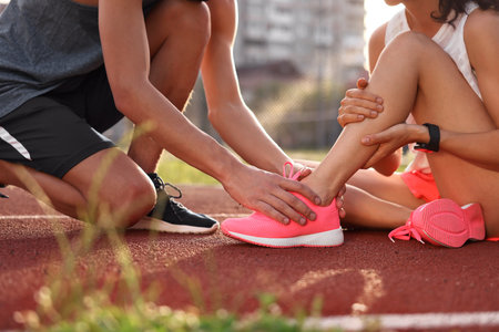 Sports injury. Man helping woman with leg pain at stadium, closeupの写真素材