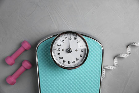 Bathroom scale, measuring tape and dumbbells on gray textured background, flat layの写真素材