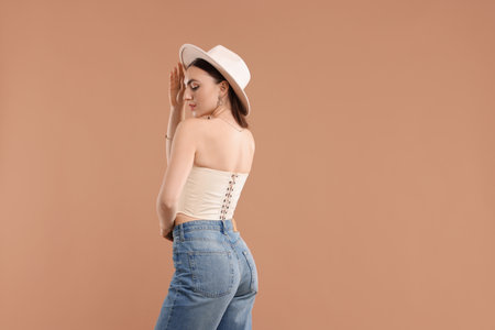 Beautiful woman in stylish corset and hat posing on beige background. Space for textの写真素材