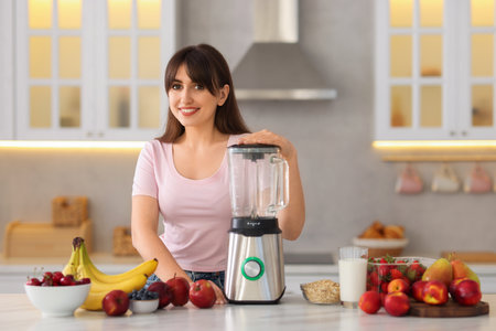 Young woman making delicious smoothie with blender at white marble table in kitchenの写真素材