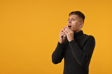 Cold symptoms. Sick man with tissue sneezing on orange background, space for textの写真素材