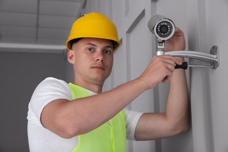 Technician with screwdriver installing CCTV camera on wall indoorsの写真素材
