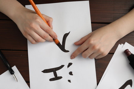 Calligraphy. Woman with brush writing words River and Entrance in Chinese on paper at wooden table, top viewの写真素材