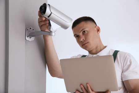 Technician with laptop installing CCTV camera indoorsの写真素材