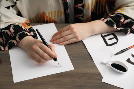 Calligraphy. Woman with fountain pen writing at wooden table, closeup. Word Speak in Chinese on paperの写真素材