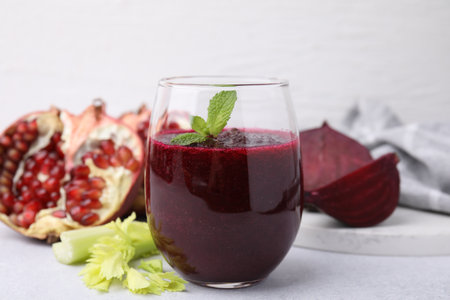 Tasty beetroot smoothie with mint in glass, fresh vegetables and pomegranate on light table, closeup. Vegan drinkの写真素材