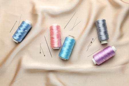 Spools of sewing threads, pins and needles on beige cloth, top viewの写真素材
