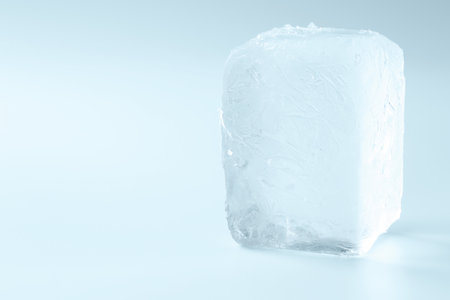 Cube of clear ice on light blue background, space for text