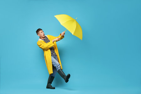 Young man with yellow umbrella on light blue background, space for textの写真素材