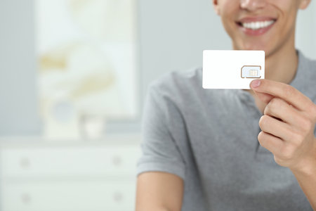Man with SIM card at home, closeup. Space for text