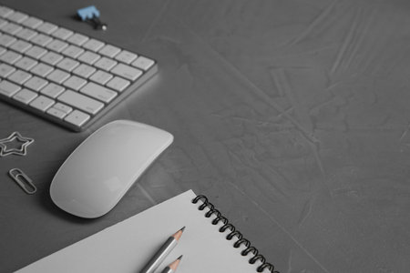 Wireless mouse, notebook, pencils and computer keyboard on grey textured table, closeup. Space for...