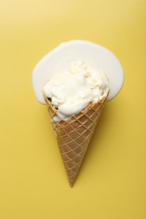 Melted ice cream in wafer cone on yellow background, top viewの写真素材