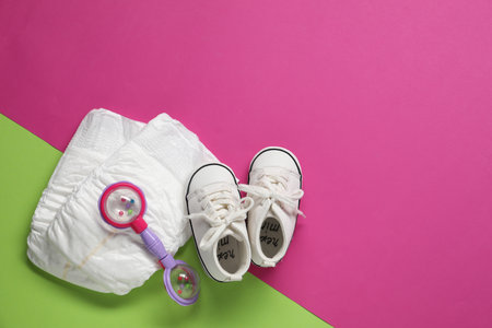 Baby rattle, boots and diapers on color background, top view. Space for text