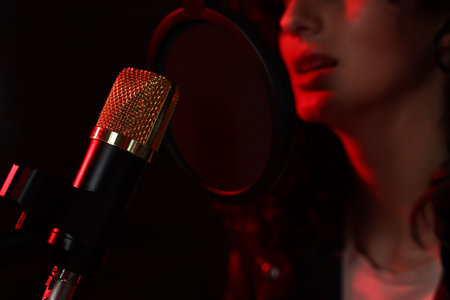 Woman singing into microphone in professional record studio with red light, closeupの写真素材