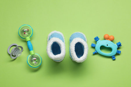 Colorful rattles, knitted boots and pacifier on green background. Baby accessories