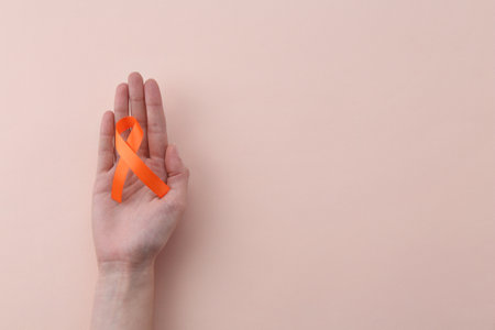 Woman with orange awareness ribbon on beige background, top view. Space for textの写真素材