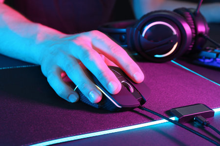 Gamer using modern wired computer mouse in neon lights at dark table, closeupの写真素材