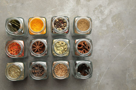 Different spices in glass jars on gray table, flat lay. Space for textの写真素材