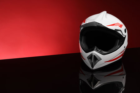 Modern motorcycle helmet with visor on mirror surface against red background. Space for textの写真素材