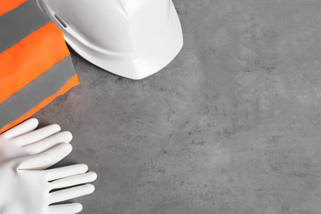 Reflective vest, hard hat and protective gloves on gray background, flat lay. Space for text