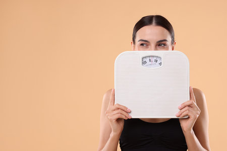 Diet and weight loss concept. Young woman with floor scale on beige background. Space for textの写真素材