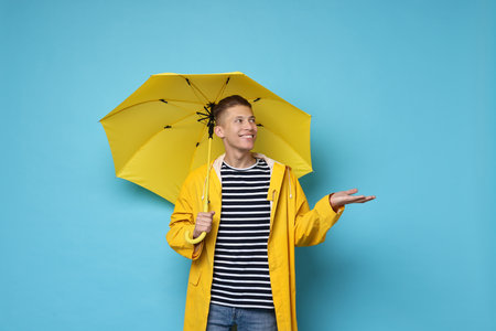 Young man with yellow umbrella on light blue backgroundの写真素材
