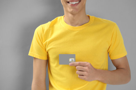 Man holding SIM card on grey background, closeup