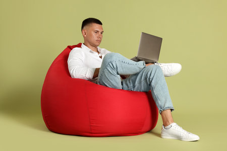 Handsome man with laptop on red bean bag chair against green backgroundの写真素材