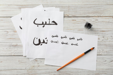 Calligraphy. Papers with words Milk and Antelope in Arabian language, inkwell and brush on white wooden table, flat layの写真素材