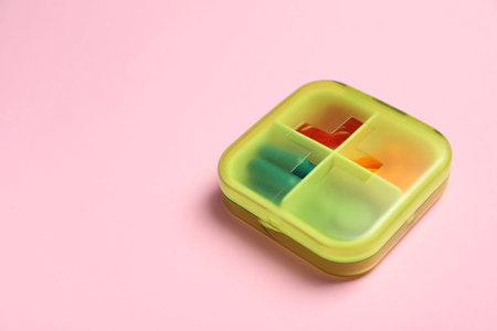 Different pills in organizer on pink background, space for textの写真素材
