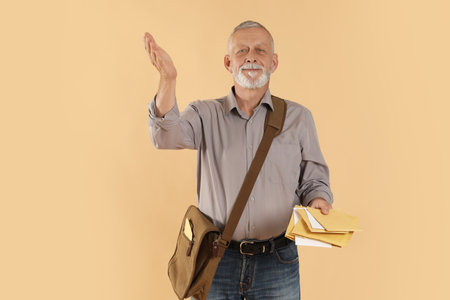 Happy postman with brown bag delivering letters on beige backgroundの写真素材