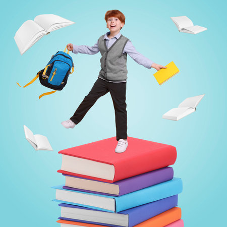 Happy schoolboy with backpack and textbook on stack of books against light blue background. Back to schoolの写真素材
