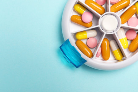 Different pills in organizer on light blue background, top view. Space for text
