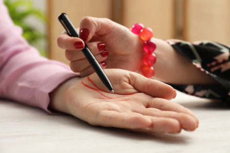 Fortune teller reading lines on woman's palm at white wooden table, closeup. Chiromancyの写真素材