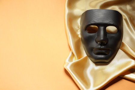 Theater arts. Black mask and golden fabric on pale orange background, top view. Space for textの写真素材