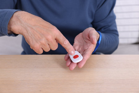 Senior man with emergency call button at wooden table, closeup
