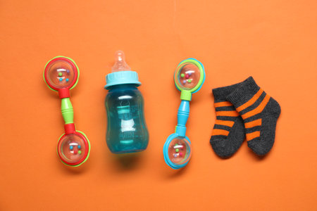 Colorful rattles, bottle and socks on orange background, flat lay. Baby accessoriesの写真素材