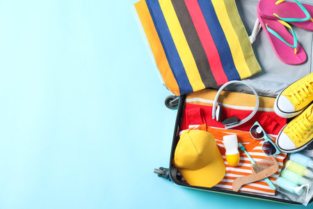 Open suitcase with traveler's belongings on light blue background, top view. Space for textの写真素材