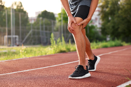 Sportsman with leg injury suffering from knee pain at stadium, closeup. Space for textの写真素材