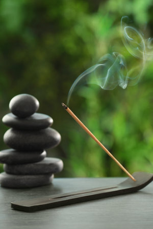 Incense stick smoldering in holder and spa stones on wooden table outdoors. Om ligatureの写真素材