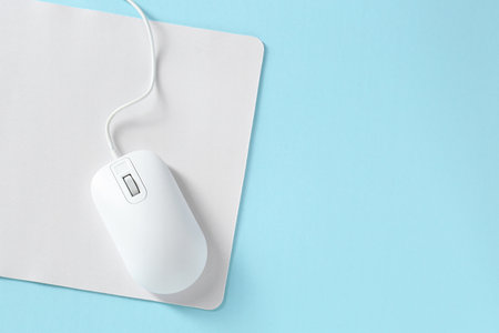 Wired mouse and mousepad on light blue background, top view. Space for text