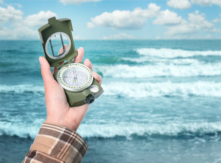 Woman holding compass on beach near sea, closeup. Space for textの写真素材