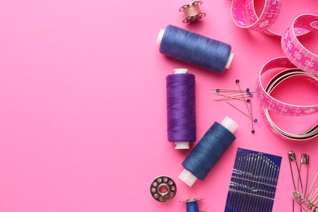 Flat lay composition with different sewing supplies on pink background. Space for text